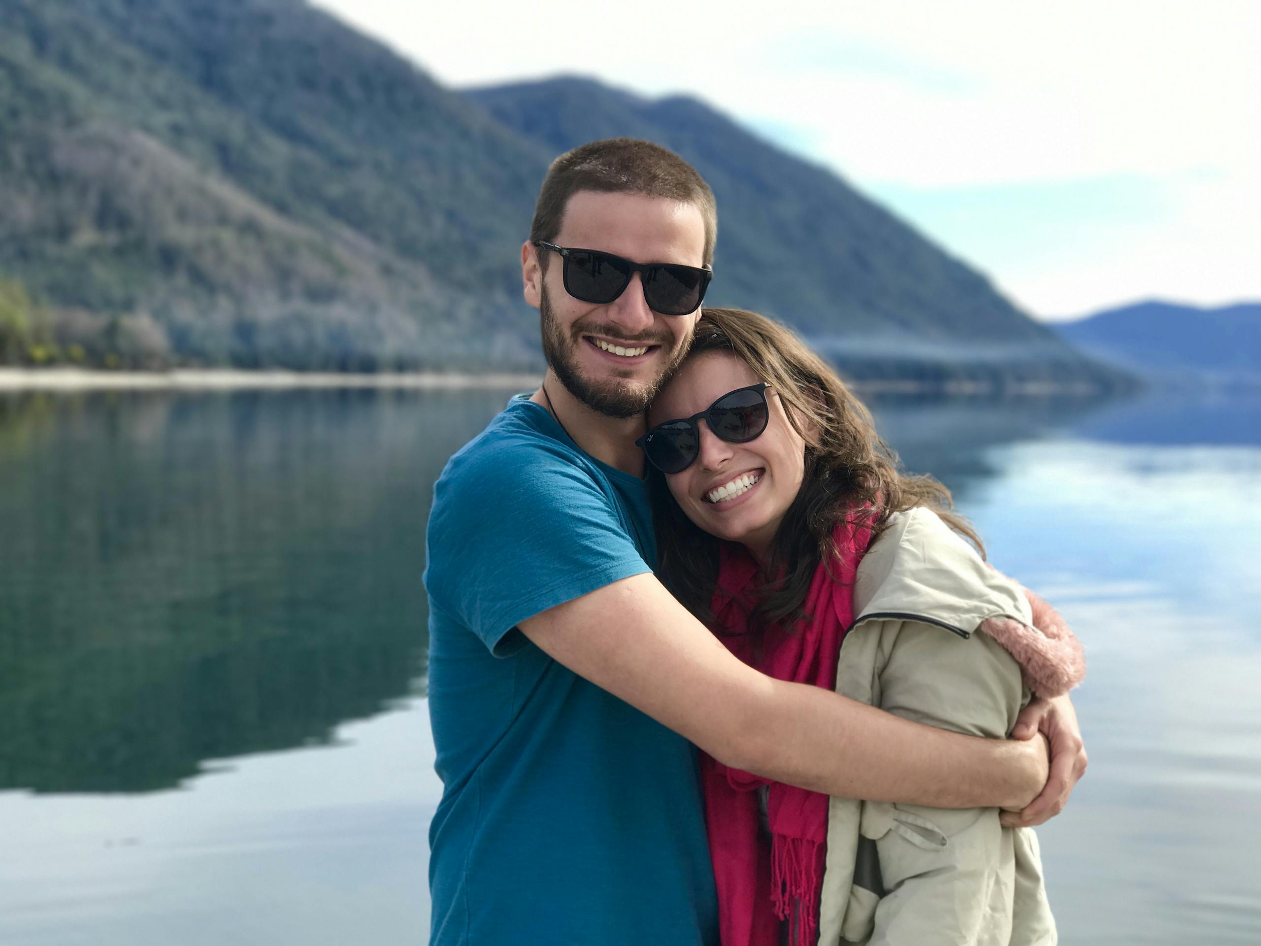 A joyful couple shares a warm embrace by a serene mountain lake, symbolizing love and togetherness.